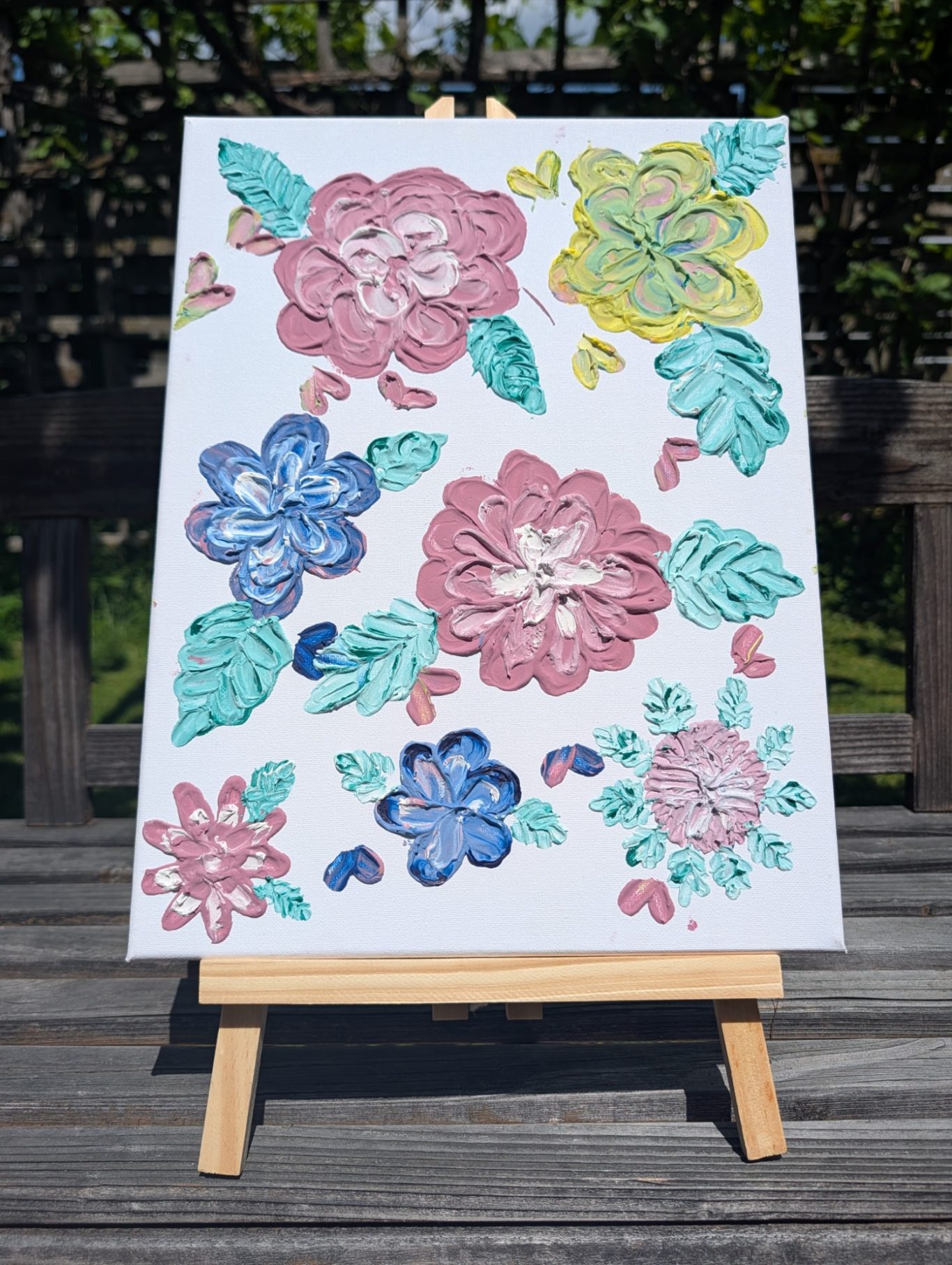 Blumenland Buntes Blumenmuster auf einer Leinwand, umgeben von grünen Blättern.