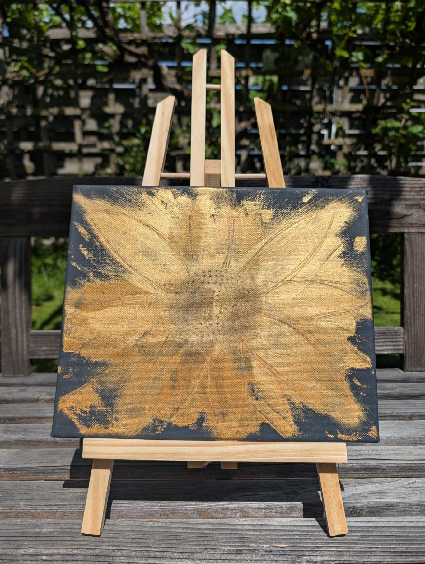 Sonnenblumen Gold Ein goldenes Sonnenblumenbild auf einer Staffelei, vor einem Holzhintergrund.
